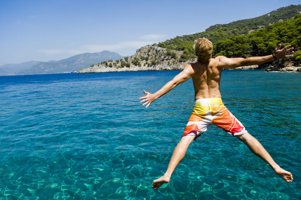 Young,Man,Jumping,Off,A,Boat,,Enjoying,The,Freedom,Of